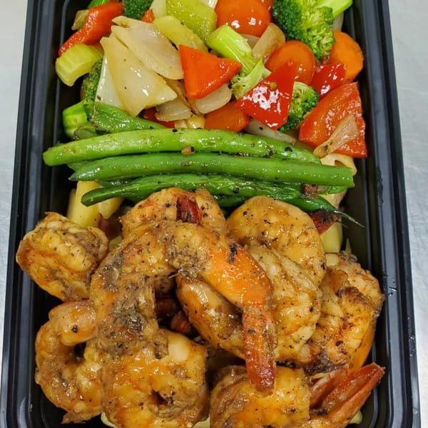 Jamaican jerk shrimp with green beans, broccoli, carrots, and bell peppers in a black to-go container.