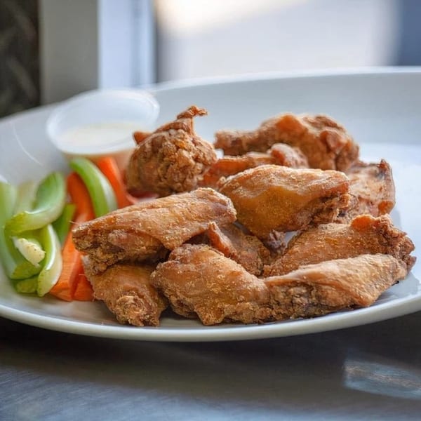 A plate of crispy fried chicken wings with celery, carrots, and a side of ranch dressing.