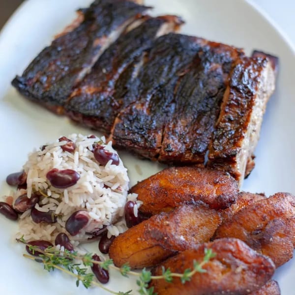 Jammin Island BBQ ribs with rice and peas, fried plantains, and a thyme garnish.