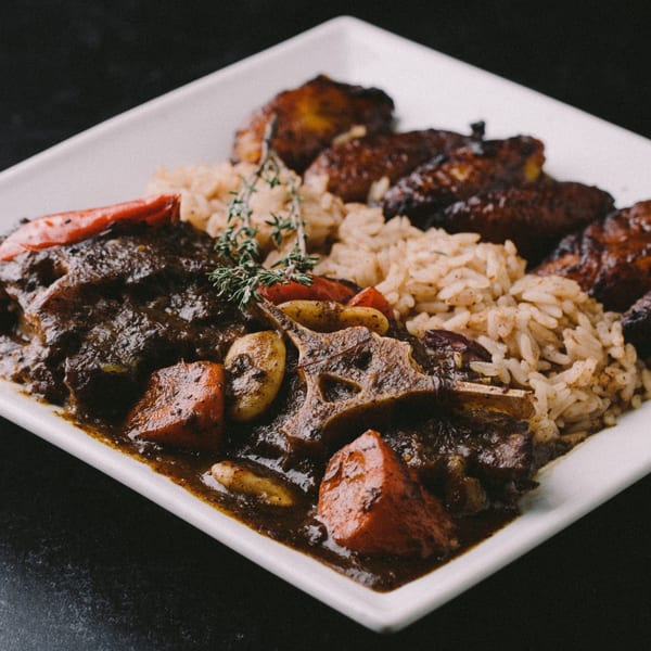 Jamaican oxtail stew with rice and peas, plantains, and thyme on a white plate.